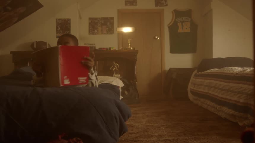 A boy in his room laying on the bed writing on a notebook