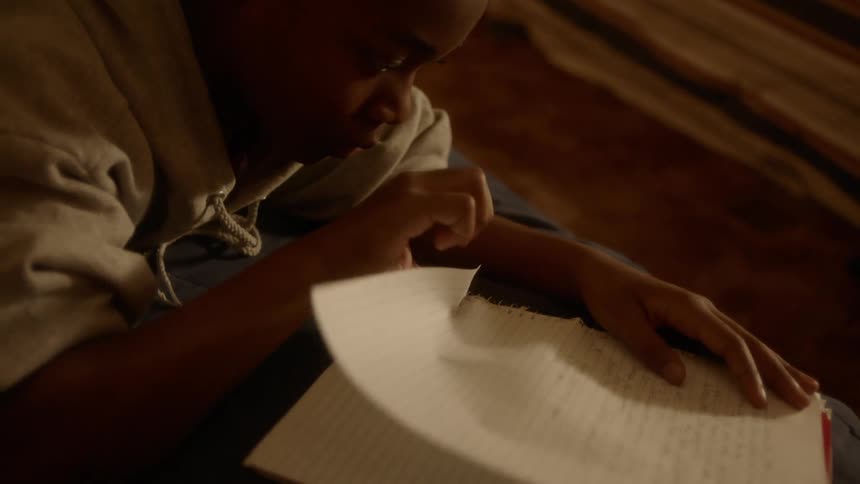 A young male is writing in a spiral bound notebook and tears the page out that he is working on