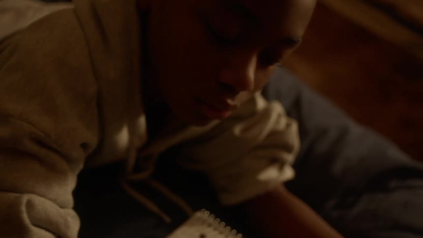 A boy writing in a notebook while laying on a bed