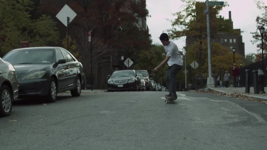 A teenage boy does a skateboard trick in the middle of a street in an urban neighborhood