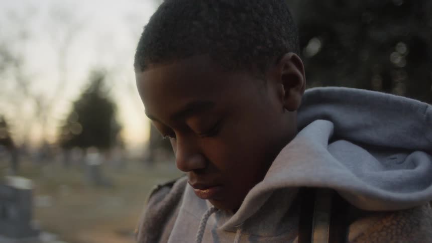 Boy contemplates while standing in graveyard during the day
