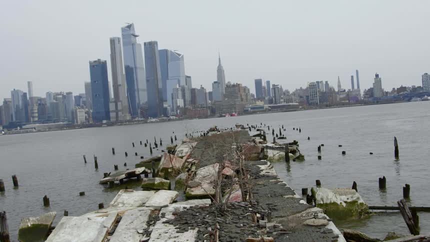 An abandoned pier is broken and in complete disrepair across the water from a metropolitan area