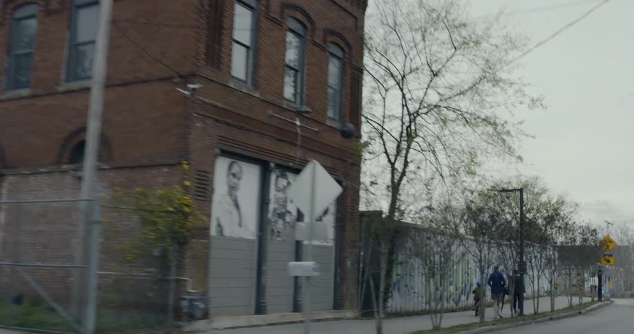 Families walk together on a sidewalk next to walls covered with graffiti on a cloudy day