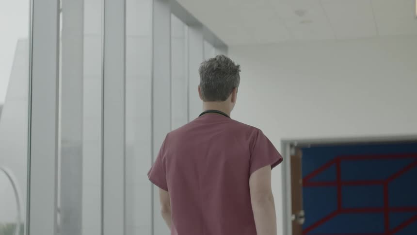 A male medical professional walks along a brightly lit corridor