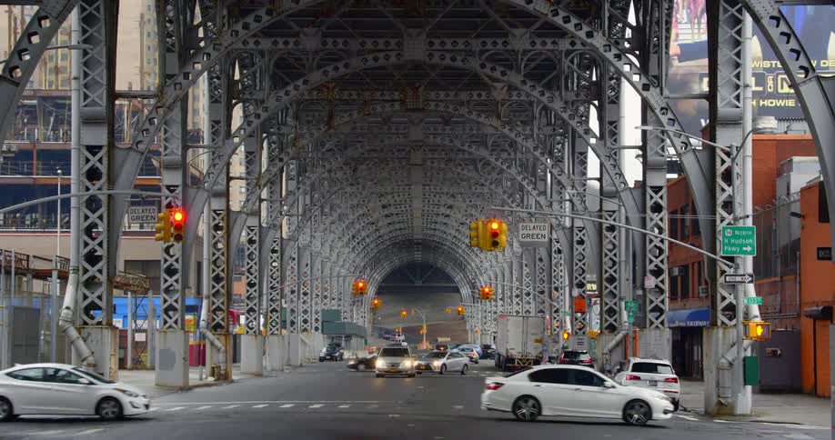 Vehicles pass through an intersection under a large city bridge