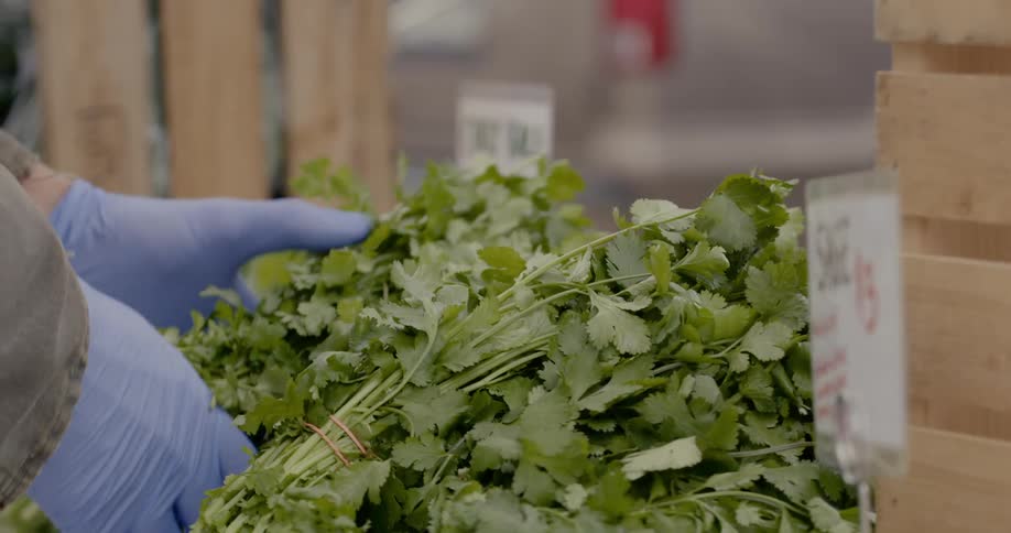 A person wearing gloves taking vegetables from a wooden crate and stacking them on a table