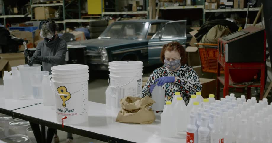 People sitting at a table bottling liquid from larger pails