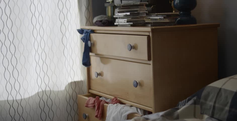 A dresser with clothes spilling out of the drawers and a cd player on top