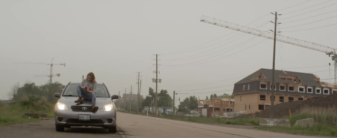 A person sits on the hood of their car