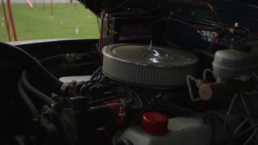 The engine of an old vehicle that is parked next to a lawn with waving american flags