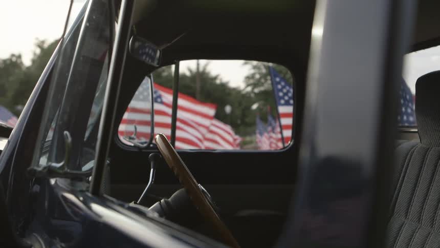 Looking through the window of a pickup truck at a bunch of american flags in the field