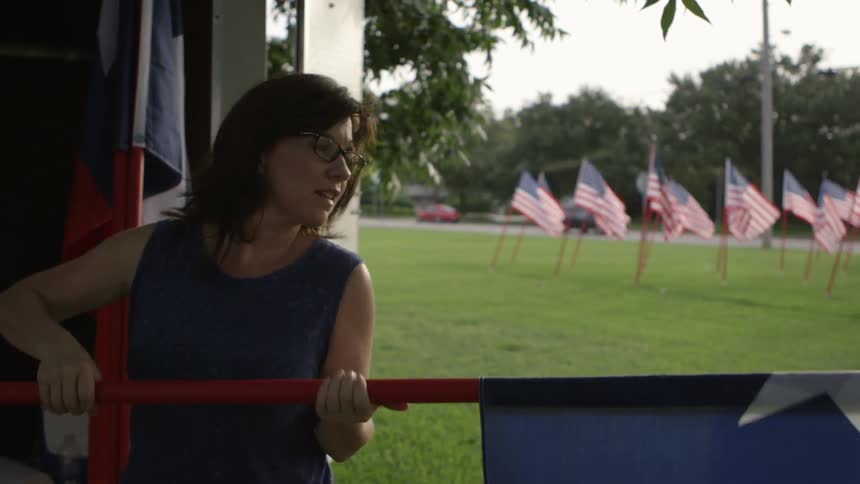 A woman rolls up a state flag with rows of american flags billowing in the background