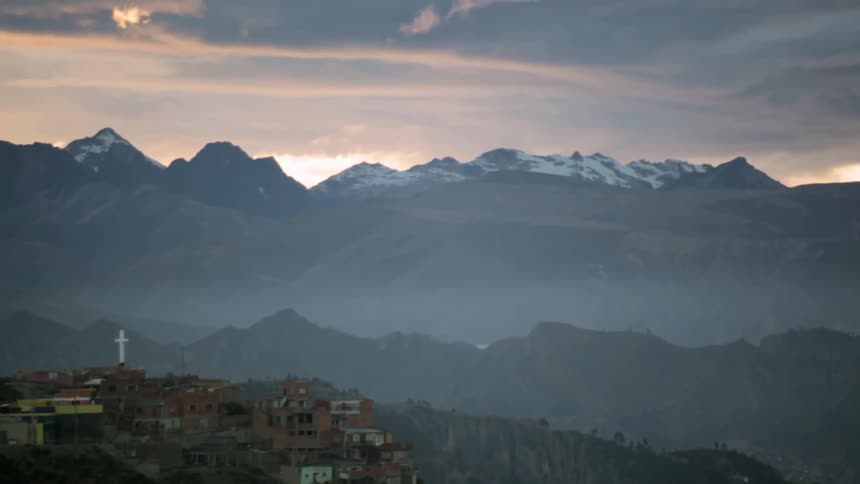 View of a town and a church cross located near snow-capped mountains on a cloudy day