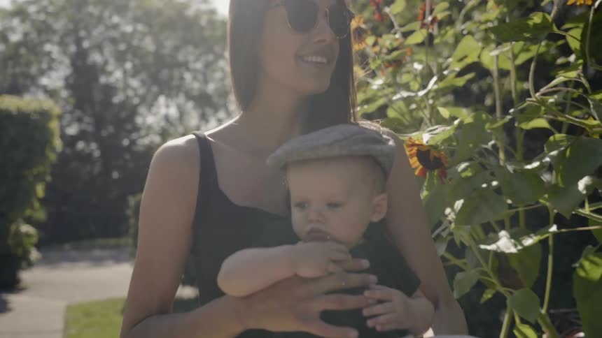 A mom smiles as she carries her son and looks at sunflowers in a garden