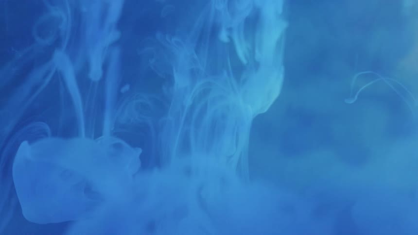 Drops of a lighter hued blue liquid flow and descend lower in a dark blue liquid while swirling and mixing
