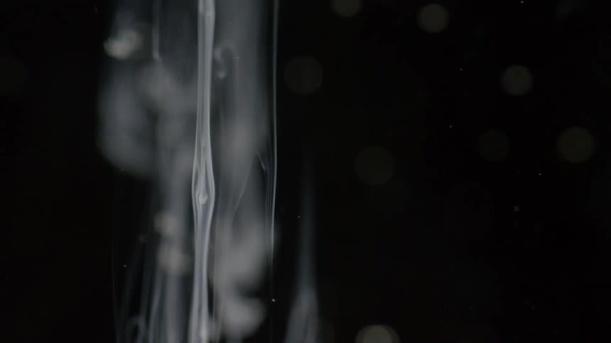 A stream of white cloudy liquid sinks and oozes down with dots of light against black