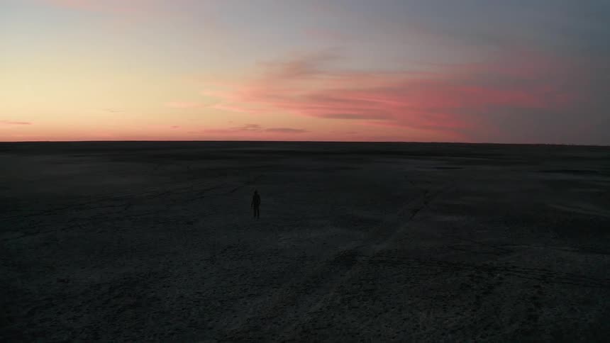 A man walks through a large flat field at sunset