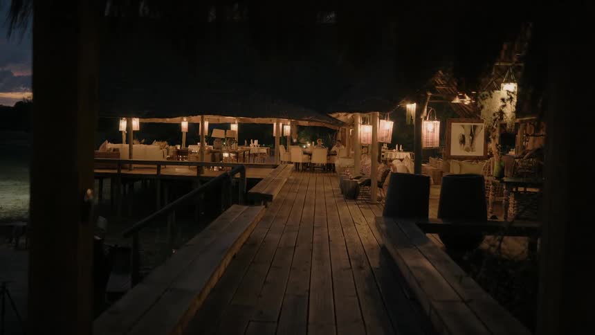 Lanterns hang in a covered dining area on a wooden deck on the beach at night