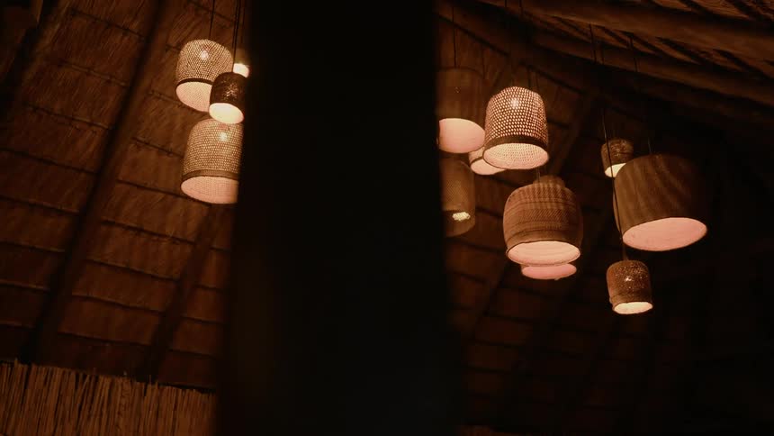 Woven bamboo lights in various sizes hanging from rafter in outdoor hut