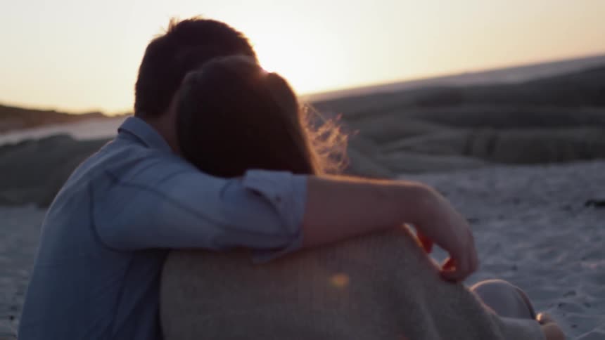 A man and woman sit together at the beach
