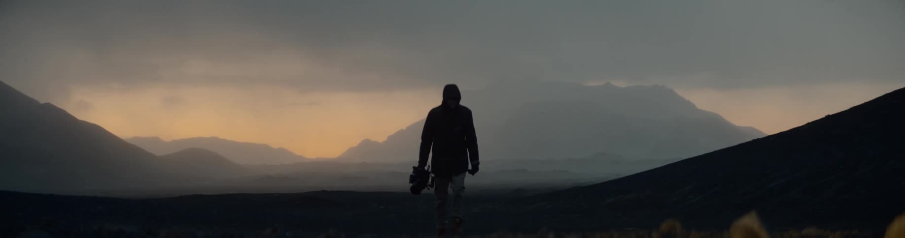 Mans silhouette carrying a professional camera walks along the way in the field