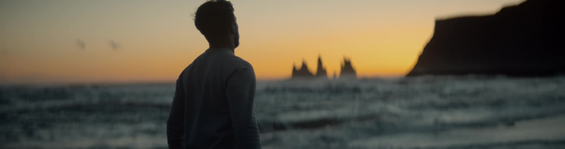 Mans silhouette walks along the sand beach at sunset next to the sea
