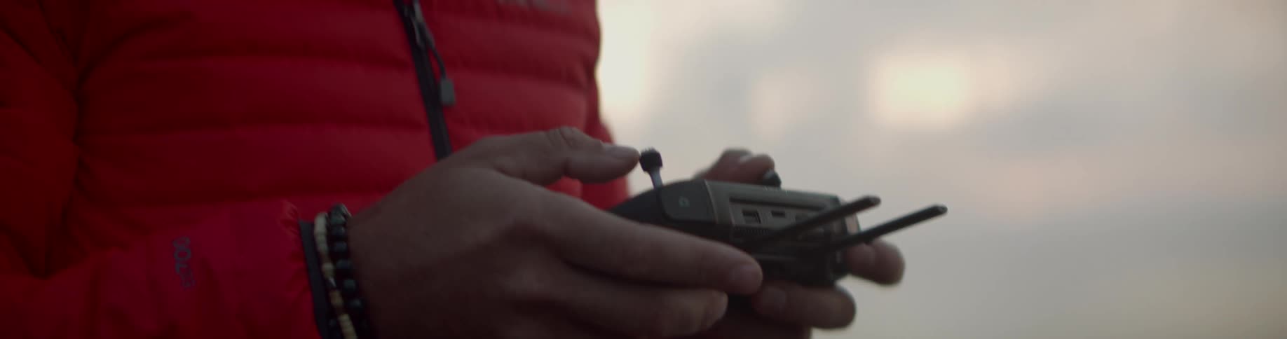 Wearing knit cap and red jacket a man operates drone controller outdoors
