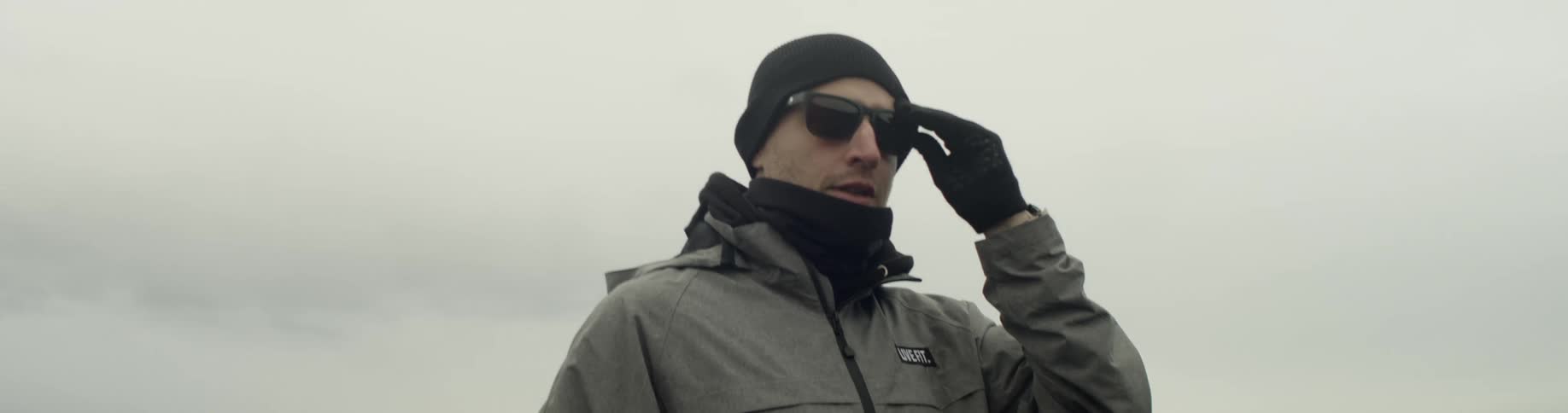 Man wearing sunglasses walks on the black sand on a cloudy day