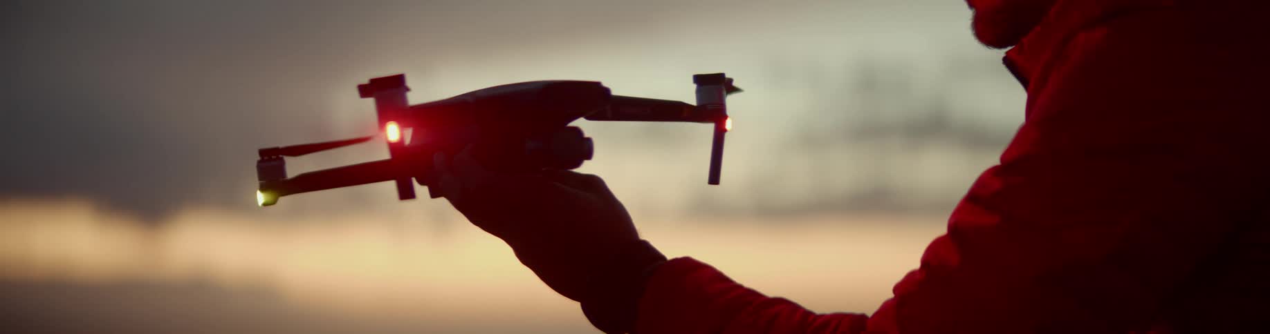 A man is holding a drone at sunset