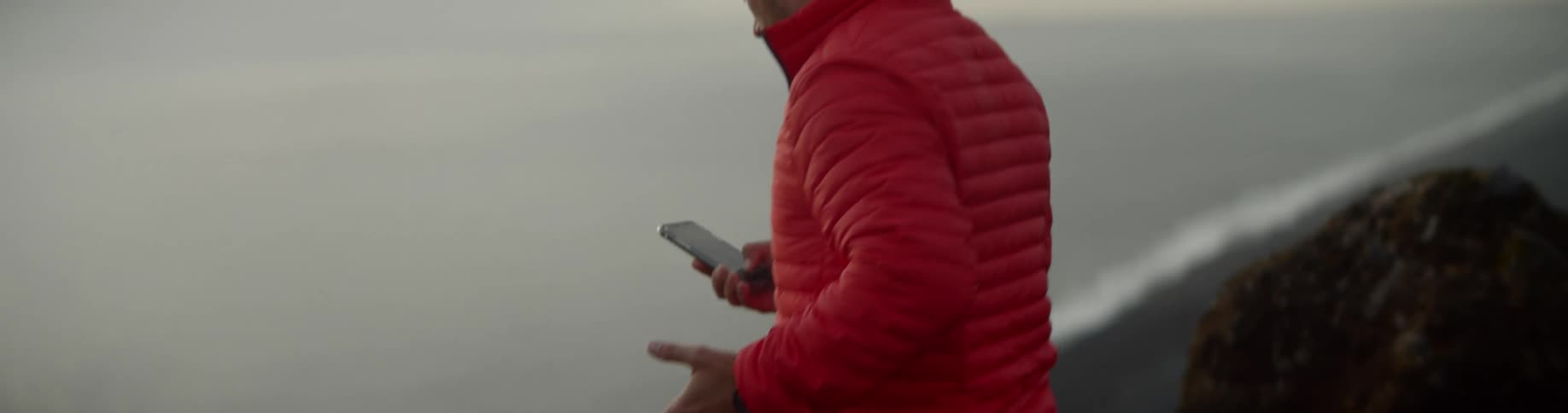 Man stands on high cliff above ocean making a video call