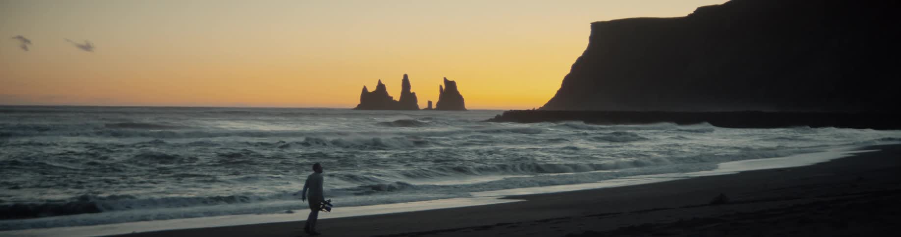 Man walks along the beach toward cliff at sunset