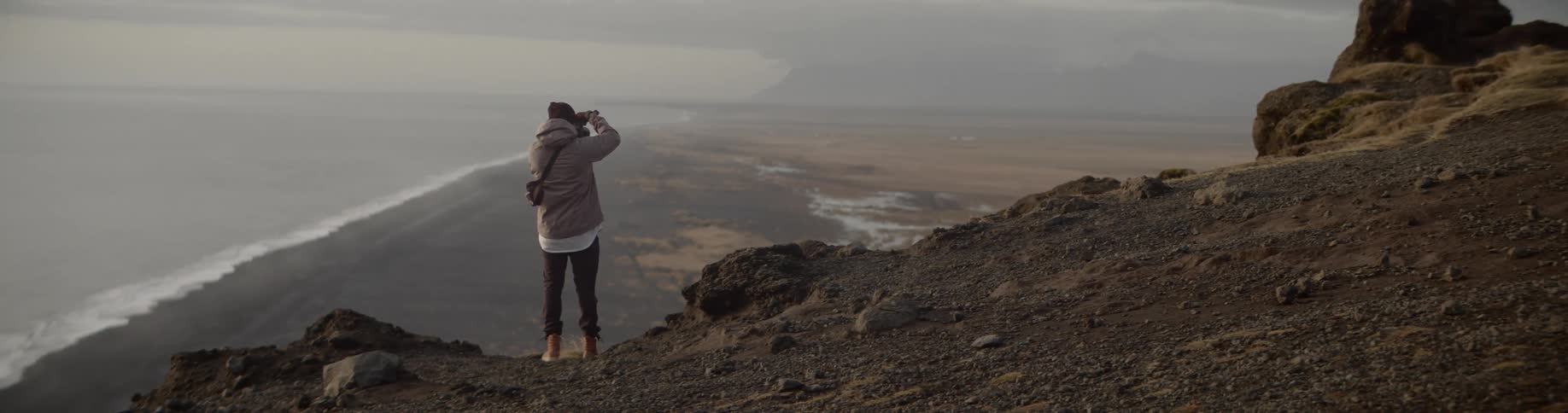 Man standing on the edge of the cliff takes a picture of the seashore