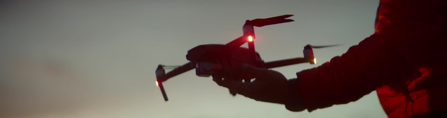 Person in red coat holds small drone at dusk
