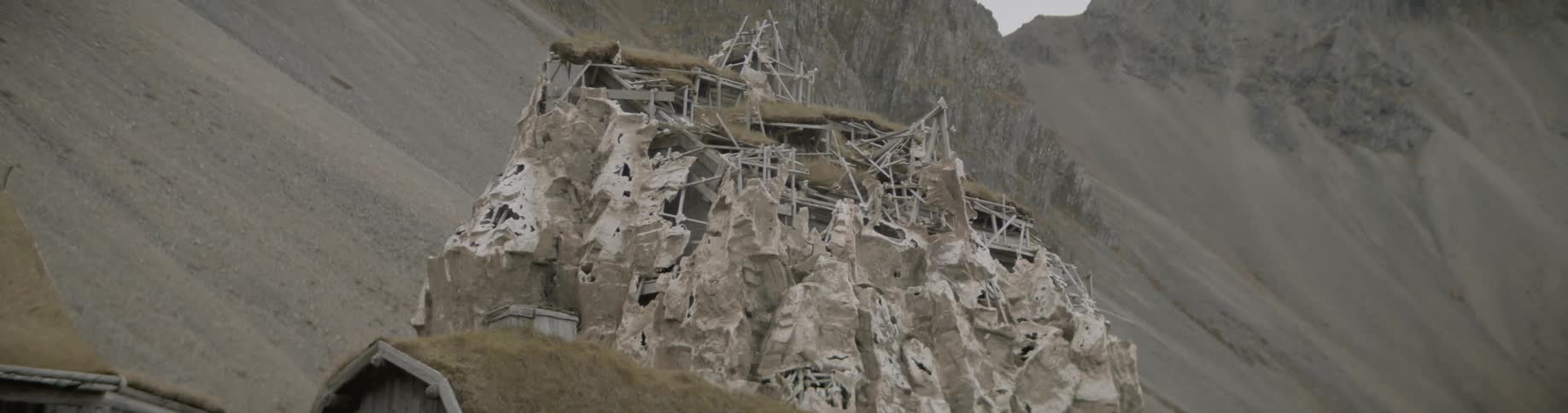 Mud hut with grass roof stands in front of sandy mountains