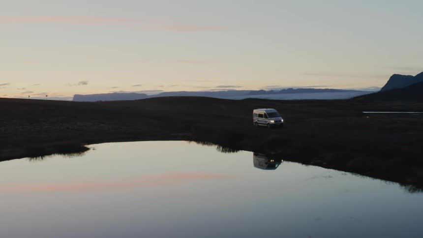 Van driving at the top of mountain near lake at sunset