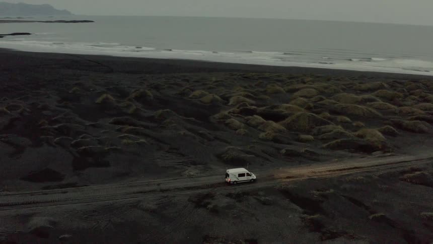 A white van slowly navigates along a dirt road nearby the ocean shoreline