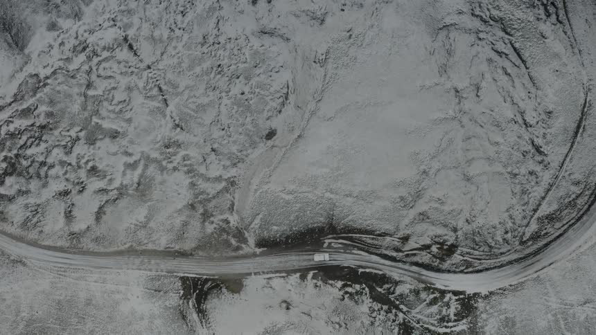 Aerial view of a car driving on a snowy mountain road