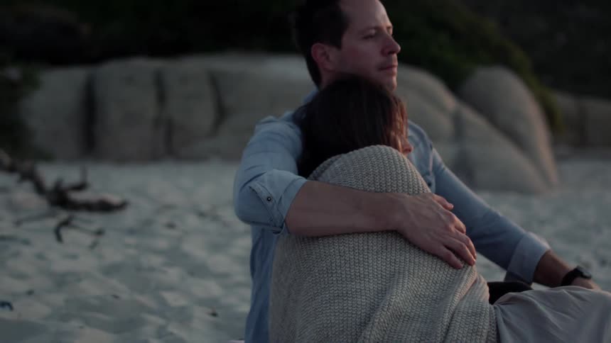 A man and woman cuddle on the beach