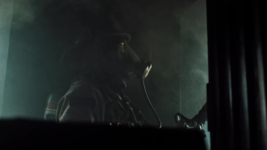 A firefighter uses a hose on a fire in another room