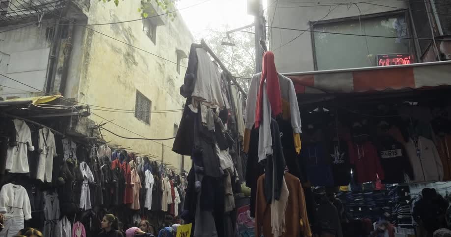 Multiple items of clothing hang outside of small stores on a busy street