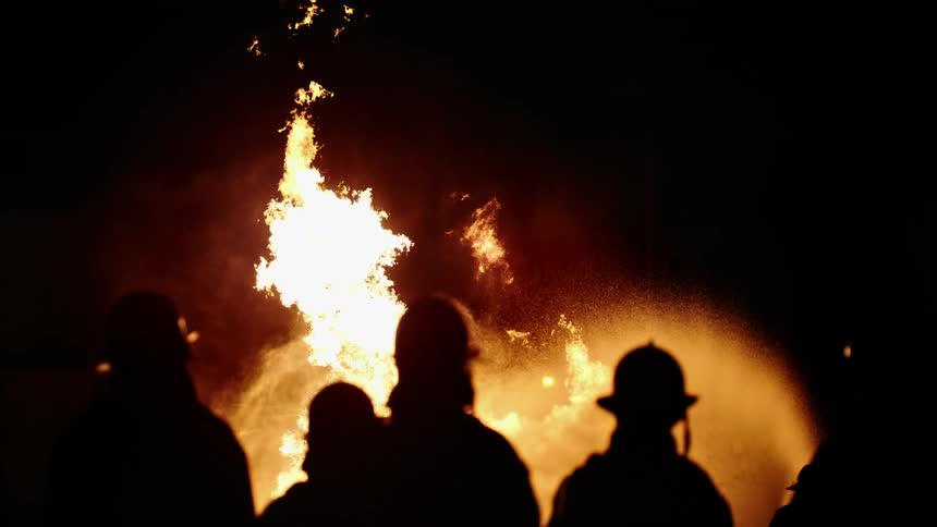 Firefighters are gathered as fire engulfs the night sky