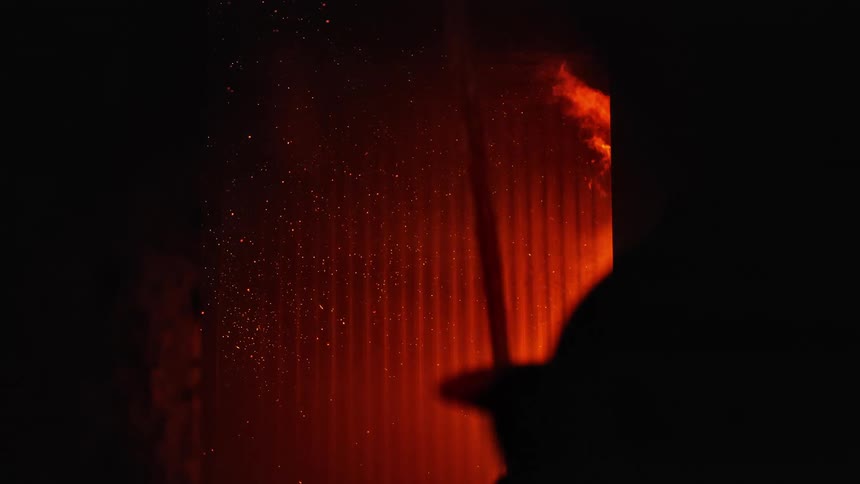 Firefighters working in the darkness turn on a fire hose to spray water on a raging fire