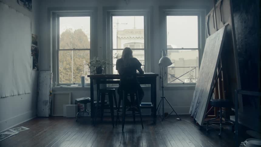 Man sits on stool at table in art studio near windows