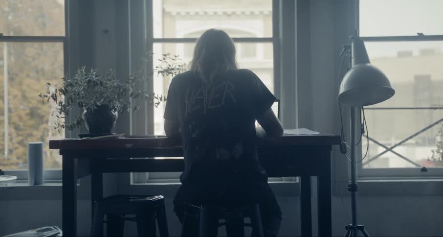 A woman sits at a desk in front of large windows