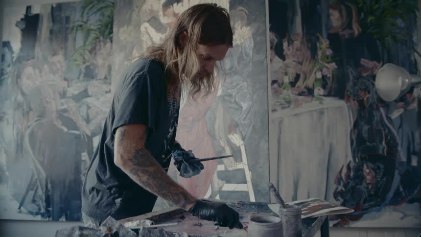 Long haired man paints a large canvas in a room