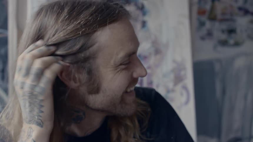 Long hair blonde man sitting in front of the painted wall laugh