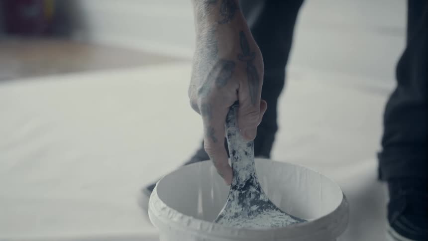 A person dips a wide paint brush into a paint bucket