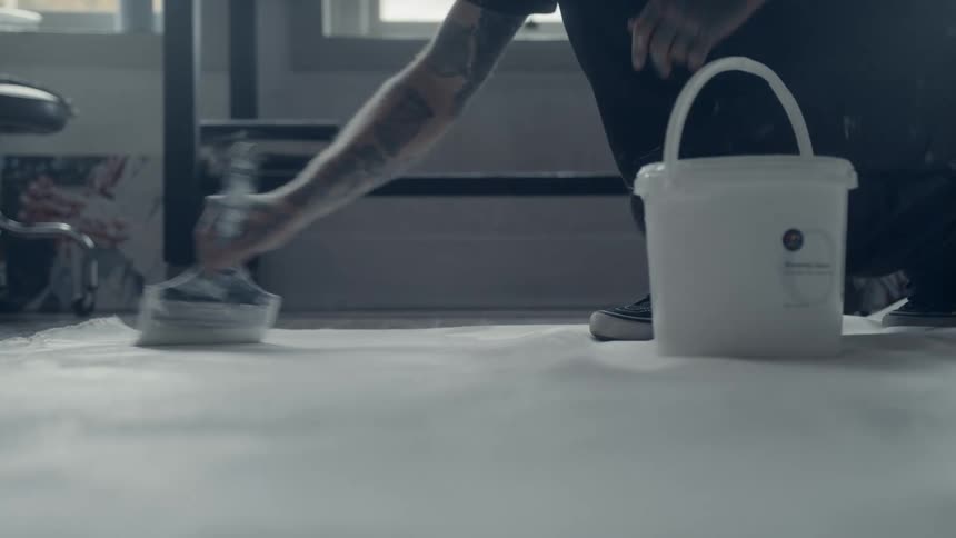 Tattooed person paint the floor of a house with a brush