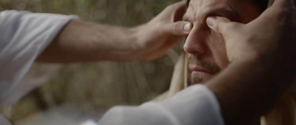 A man rubs another mans eyes with his thumbs