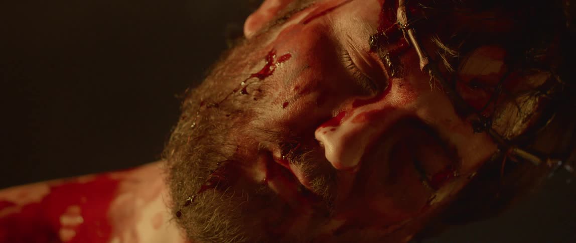 A man covered in blood lies with his eyes closed